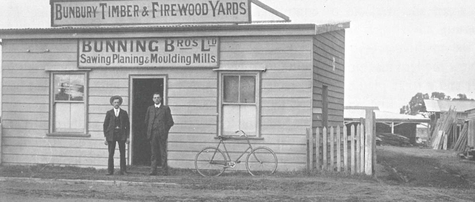 Black and white photo of two men standing in front Bunnings Co building