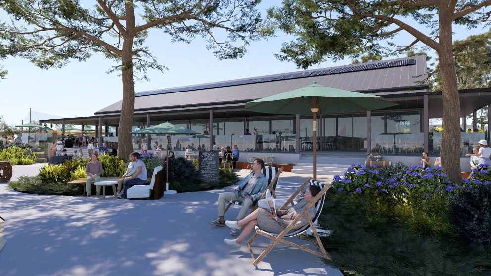 Outdoor café seating with people relaxing under umbrellas, surrounded by trees and coastal planting.