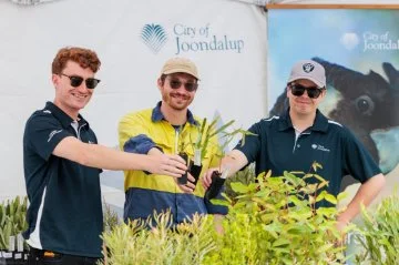 Three City of Joondalup staff holding native seedlings at a community plant giveaway display.