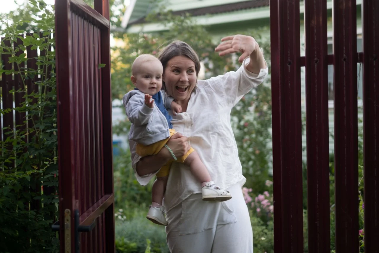 A woman holding a baby waving at someone