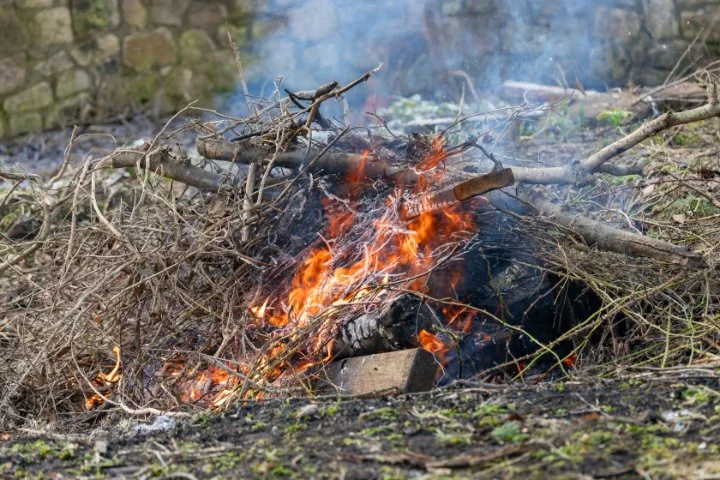 Small pile of garden branches and wood burning outdoors, with visible flames and smoke.