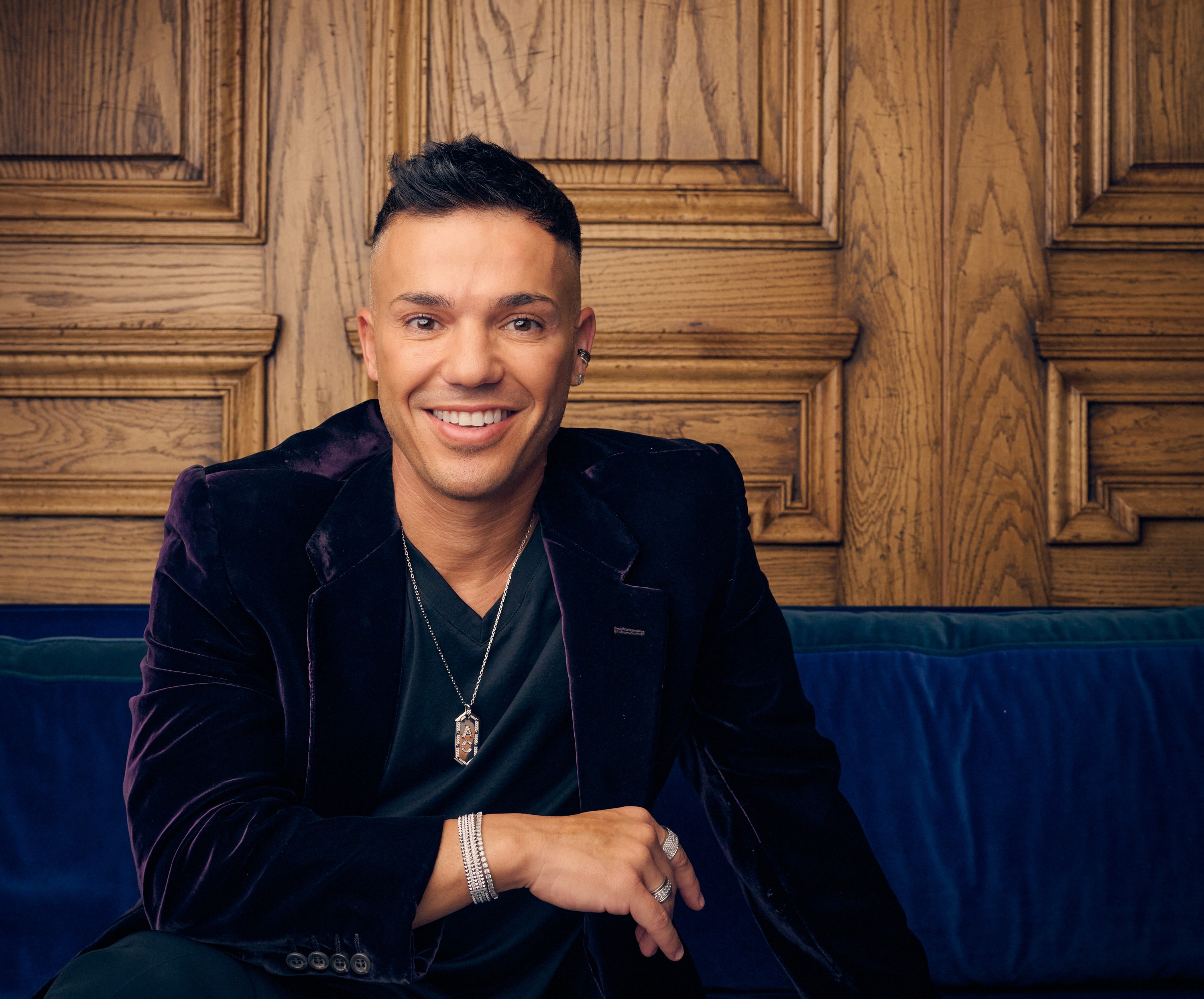 Image of artist Anthony Callea smiling and leaning forward on couch