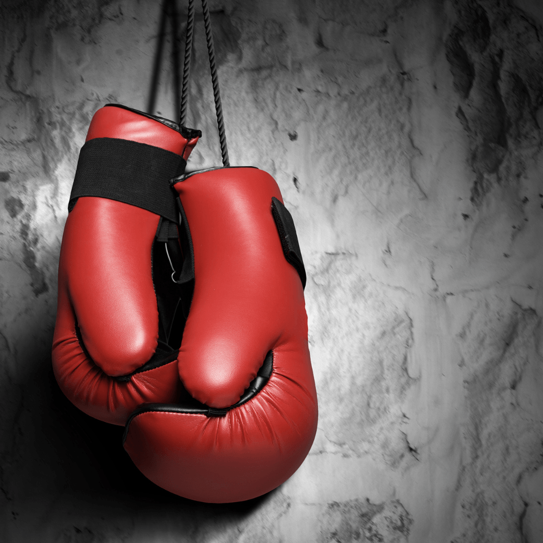 Red boxing gloves hanging by their laces against a rough gray wall.