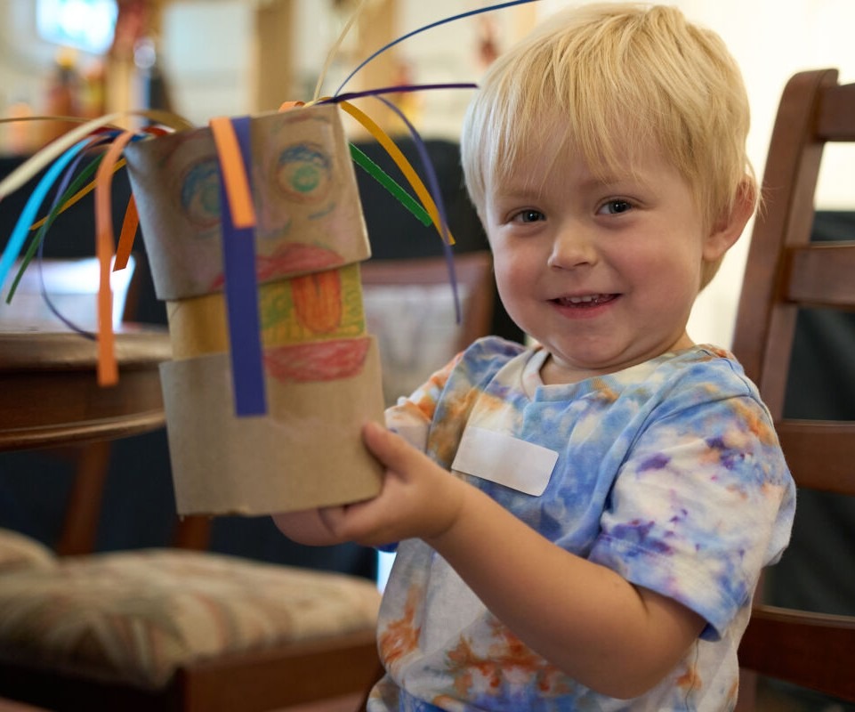 Little boy holding a craft creation smiling at the camera