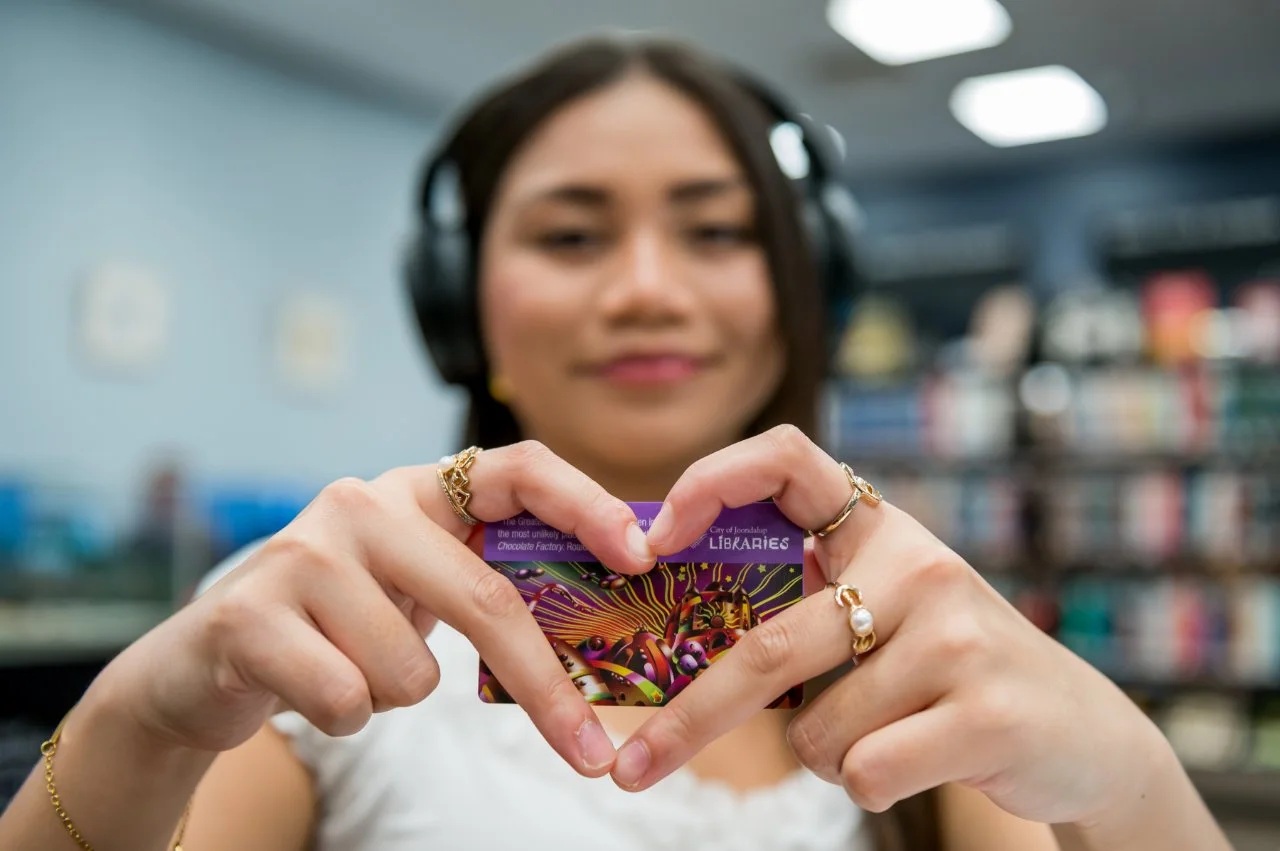 Young lady wearing heading headphones holding library card
