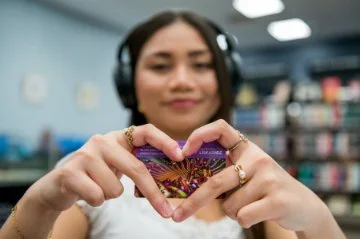 Young lady wearing heading headphones holding library card
