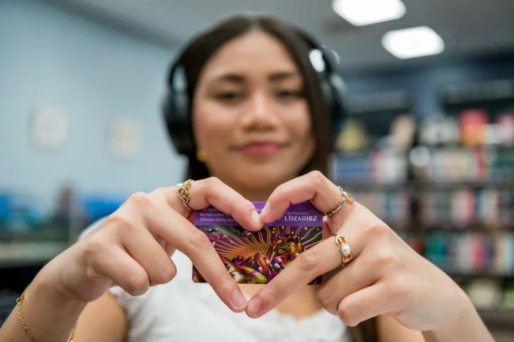 Young lady wearing heading headphones holding library card