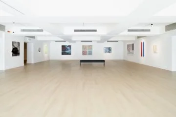Bright, modern art gallery with wooden floors, white walls, and colorful paintings displayed around the room.