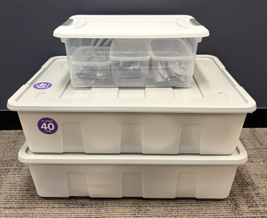 Three stacked white storage boxes with lids, the top box containing smaller clear containers.