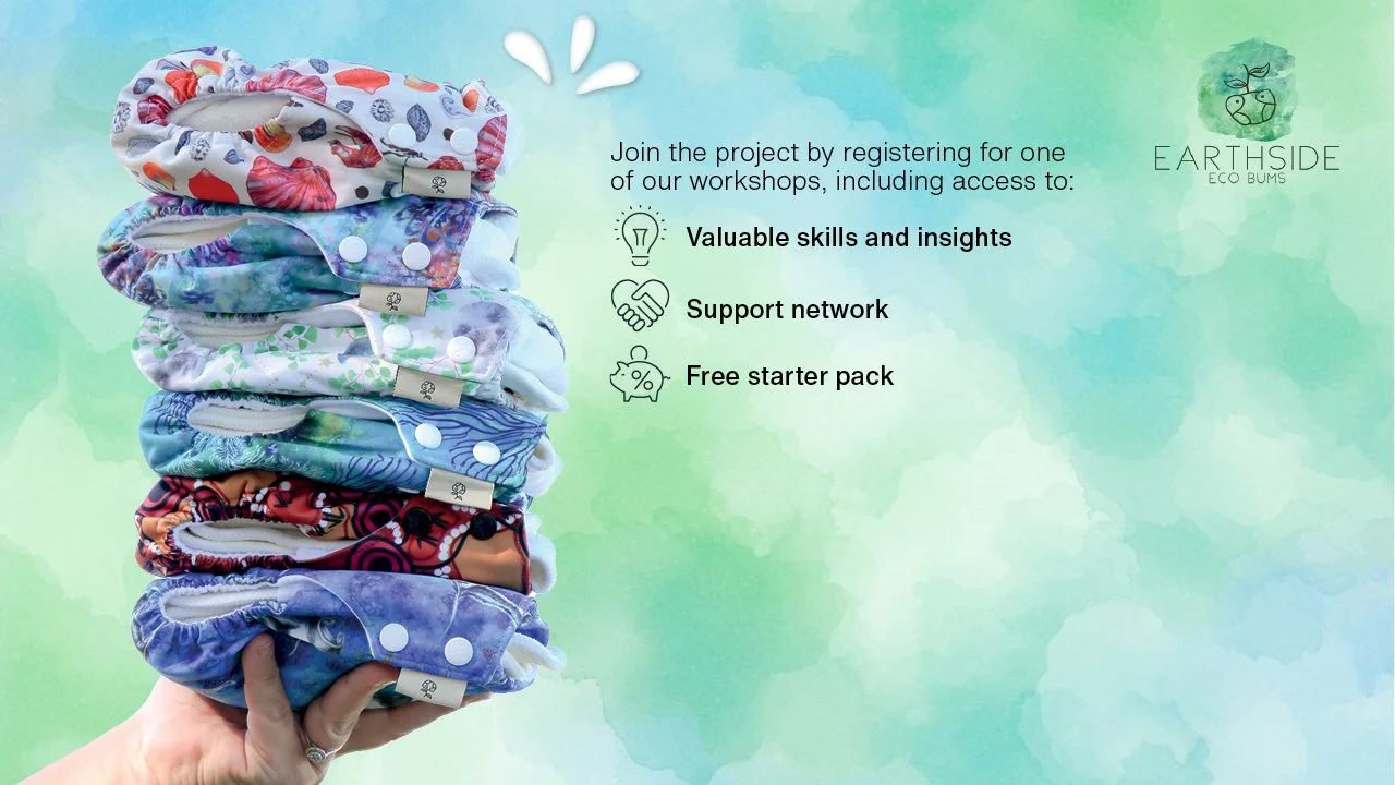 A hand holds a stack of colorful, reusable nappies against a soft green-blue watercolor background