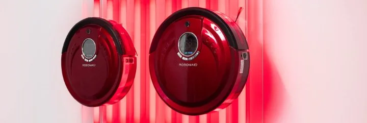 Two red robotic vacuum cleaners are mounted on a white wall with vertical red lights behind them.