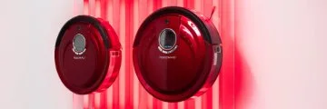 An art piece consisting of a pair of burgundy round robotic vacuums on a soft pink fluorescent background.