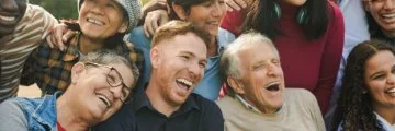 Diverse group of smiling people of different ages and backgrounds sharing a joyful moment together outdoors.