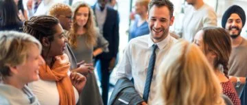 Diverse group of people smiling and chatting at a community networking or social event indoors.