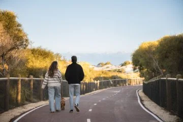 Photo of two people and a dog walking along a coastal path