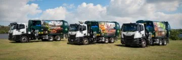 Four green and white recycling trucks parked on grass under a bright sky,